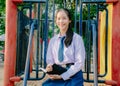 Lovely teenage girl wearing school uniform writing book while sitting on a swing at the park Royalty Free Stock Photo