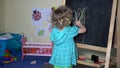 Lovely toddler girl drawing on chalkboard at home