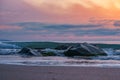 Lovely view of a beach at sunset with high tides crashing against sharp rocks under a cloudy sky