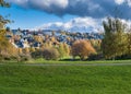 Lovely view of a green field with colorful autumn trees near a town under a bright cloudy sky Royalty Free Stock Photo