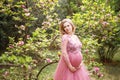 Lovely woman expecting baby in beautiful dress background of blossoming magnolia and greenery