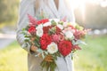 Lovely woman holding a beautiful autumn wedding bouquet. flower arrangement with white and red garden roses. Green lawn Royalty Free Stock Photo