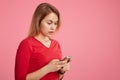 Lovely worried surprised female reads unexpected message on smart phone, wears red sweater, stands sideways against pink backgroun Royalty Free Stock Photo