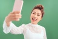 Lovely young alluring woman posting photo online, video-calling friend, holding smartphone raised as taking selfie, tilt head