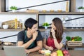 Lovely young Asian couple in modern kitchen, lover is smiling and eating fresh fruits, healthy food together on wooden table in Royalty Free Stock Photo