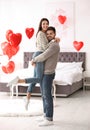 Lovely young couple in bedroom decorated with heart balloons. Valentine`s day celebration