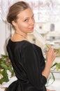 Lovely young girl in black dress with white feather is standing at window looking over her shoulder at camera. Royalty Free Stock Photo