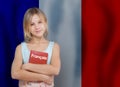 Lovely young girl holding book with inscription french in french language on flag of France background. Learn French concept Royalty Free Stock Photo