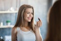 Sweet young girl looking in mirror and applying lipstick at home Royalty Free Stock Photo