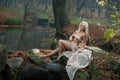 Lovely young lady sitting near river in enchanted woods. Sensual blonde with white clothes posing provocatively in autumnal park. Royalty Free Stock Photo