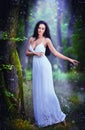 Lovely young lady wearing an elegant long white dress enjoying the beams of celestial light on her face in enchanted woods. Long Royalty Free Stock Photo