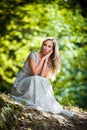 Lovely young lady wearing elegant white dress enjoying the beams of celestial light on her face in enchanted woods. Pretty blonde Royalty Free Stock Photo