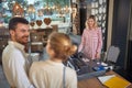 Lovely young sales person woman serving young married couple in lamp store. Couple buying home decor and lamps