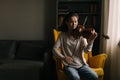 Lovely young woman plays the violin sitting on soft chair Royalty Free Stock Photo