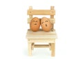 Lover eggs couple, lean on each other on wooden chair, isolated on white background