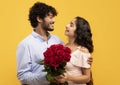 Lovers holiday. Loving indian couple holding bouquet of flowers, embracing, looking at each other on yellow background