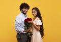 Lovers holiday. Romantic indian couple holding bouquet of flowers and looking at camera on yellow background