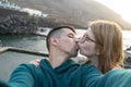 Lovers kissing with passion taking selfie in natural pool. Caucasian blonde girlfriend with glasses kiss latin boyfriend at sunset