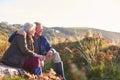 Loving Active Senior Couple Walking Along Coastal Path In Autumn Resting On Rock Together Royalty Free Stock Photo