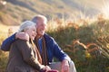 Loving Active Senior Couple Walking Along Coastal Path In Autumn Resting On Rock Together Royalty Free Stock Photo