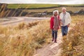 Loving Active Senior Couple Walking Arm In Arm Through Sand Dunes On Winter Beach Vacation Royalty Free Stock Photo