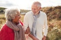 Loving Active Senior Couple Walking Arm In Arm Through Sand Dunes On Winter Beach Vacation Royalty Free Stock Photo