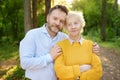 Loving adult son tenderly embracing his joyful elderly mother during walking at summer park. Mother`s day holiday