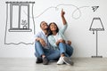 Loving african american couple imagining interior of their new flat, sitting on floor near white wall with doodle Royalty Free Stock Photo