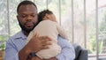 Loving African American dad embracing baby and baby girl sleeping on stepfather shoulder. Happy family with pleasure spending time