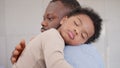 Loving African American dad embracing baby and baby girl sleeping on stepfather shoulder. Happy family with pleasure spending time