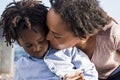 Loving african american mother kissing her little son watching video or playing game using mobile phone outdoors. Caring mother Royalty Free Stock Photo