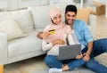 Loving arab expecting family using laptop and credit card, shopping online, sitting on floor in living room interior Royalty Free Stock Photo