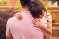 Loving Asian Father Cuddling Daughter In Garden As Girl Looks Over His Shoulder