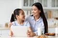 Loving asian mother and her daughter using digital tablet, looking for new recipes while sitting at kitchen table Royalty Free Stock Photo