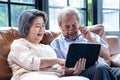 Loving Asian Senior elderly woman and old man couple sit on sofa in living room use laptop to read news and online video call with