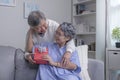 Asian senior man husband giving present gift box for Valentine`s day to happy surprised wife, sitting together on couch at home Royalty Free Stock Photo