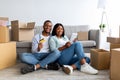 Loving black couple with digital tablet and credit card choosing furniture online after moving to new apartment Royalty Free Stock Photo