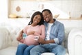 Loving black couple sitting on sofa, holding BOY and GIRL cards in hands, smiling and looking at camera at home