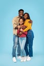 Loving black family of three embracing and smiling at camera, posing on blue background, studio shot, full length Royalty Free Stock Photo