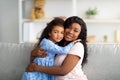 Loving black girl in pretty dress hugging her mother on sofa in living room. Strong family relationships concept Royalty Free Stock Photo