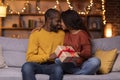 Loving black man and woman holding gift box, home interior Royalty Free Stock Photo