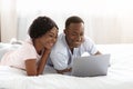 Loving black man and woman using laptop in bed