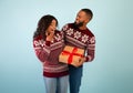 Loving black man giving Christmas gift to surprised wife celebrating xmas together, standing over blue background