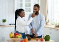 Loving black woman feeding her husband while they cooking together at kitchen Royalty Free Stock Photo