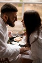 Loving Breakfast. Lovers in bathrobes share a hotel meal, gaze intertwined.