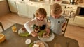 Loving brother teaching his little sister to spread chocolate nut butter on toasted bread while preparing breakfast in Royalty Free Stock Photo