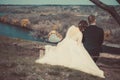 Loving couple of bride and groom, hugging, sitting on a bench, looking into the distance, against the backdrop of a village