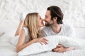 Loving couple cuddling in bed at home, hugging soft pillow, touching noses, having intimate foreplay after waking up Royalty Free Stock Photo