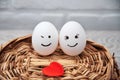 A loving couple of eggs with emoticons and a heart on a wooden basket. Royalty Free Stock Photo