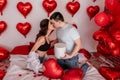 Loving couple kissing while sitting on bed decorated with heart shaped balloons. Valentines Day Royalty Free Stock Photo